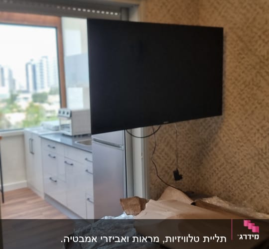 טלוויזיה תלויה על הקיר בחדר עם מטבח ברקע